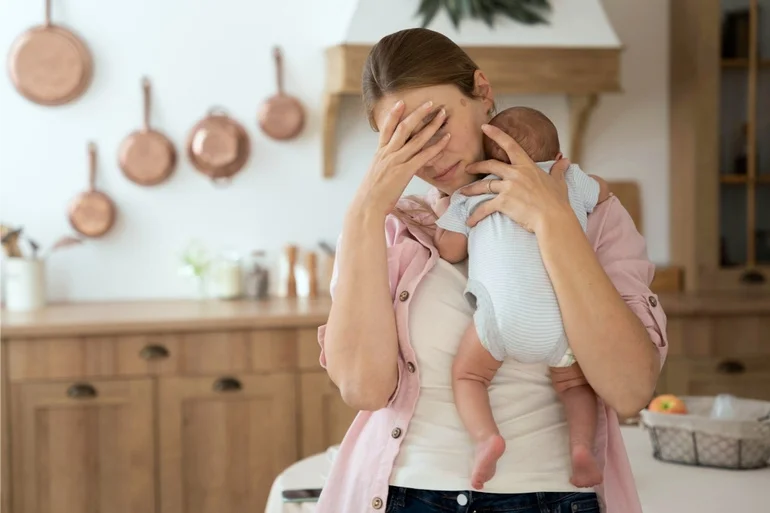 Mother holding her baby with one hand showing signs of perinatal mental health distress