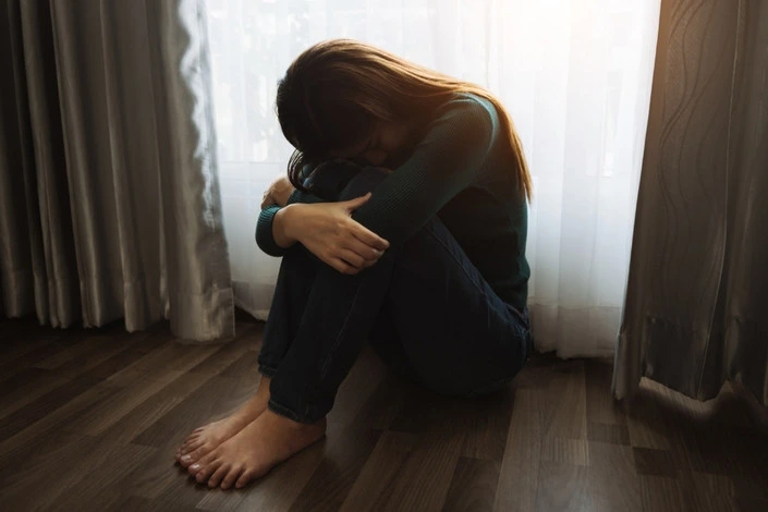 A woman sitting alone on the floor, struggling with intrusive memories or isolation.