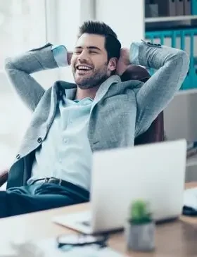 Smiling person sitting at a desk with hands on head and a laptop in front after physicatric session.