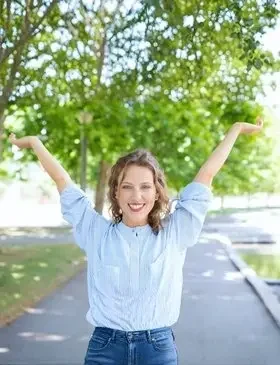 Smiling woman outdoors with arms raised, representing emotional well-being and positivity.